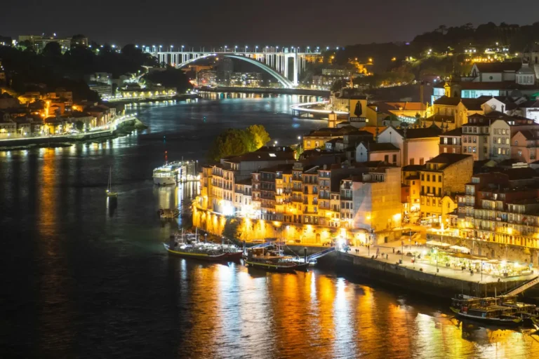 Night view of Porto waterfront with illuminated buildings and bridge reflecting on the Douro River.