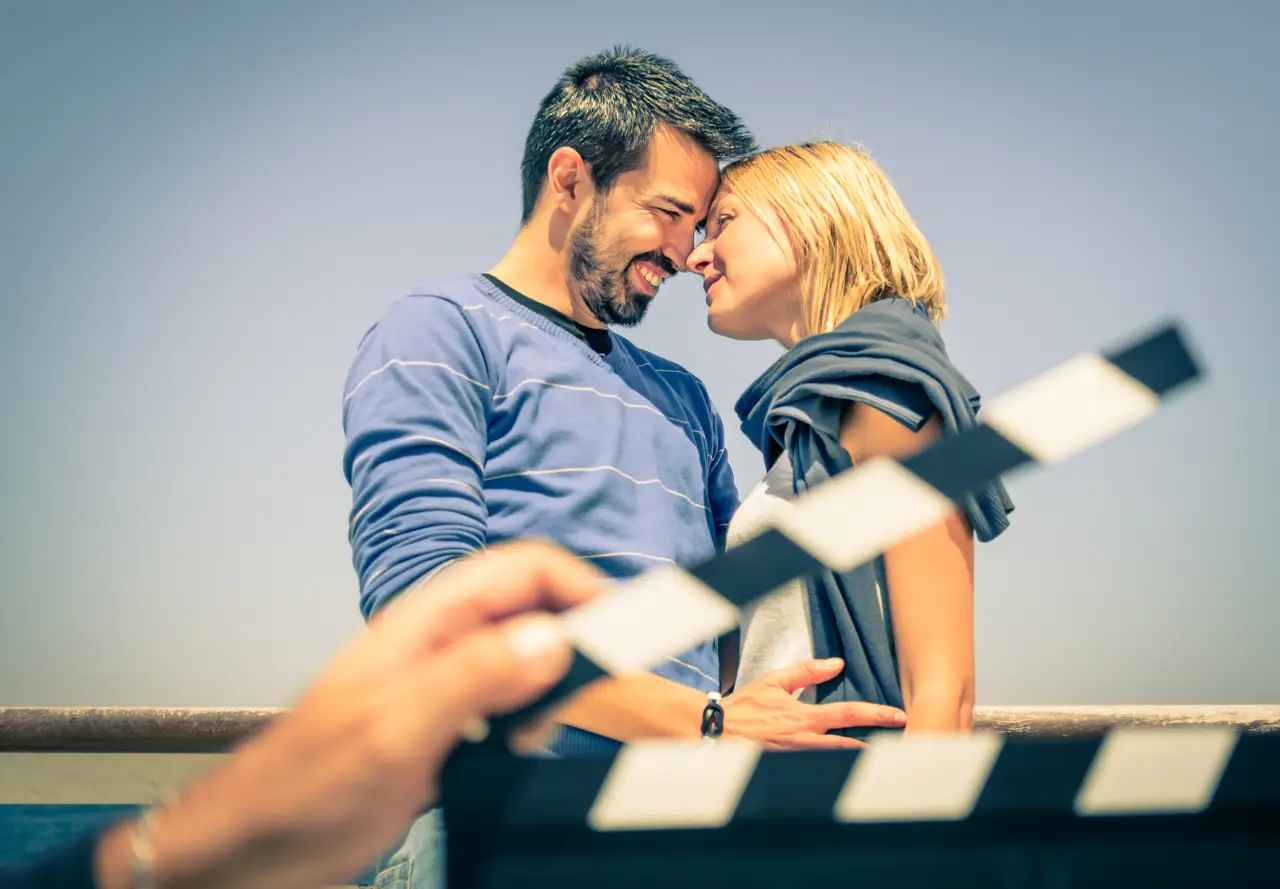 Romantic couple smiling on a film set with a clapperboard in the foreground.