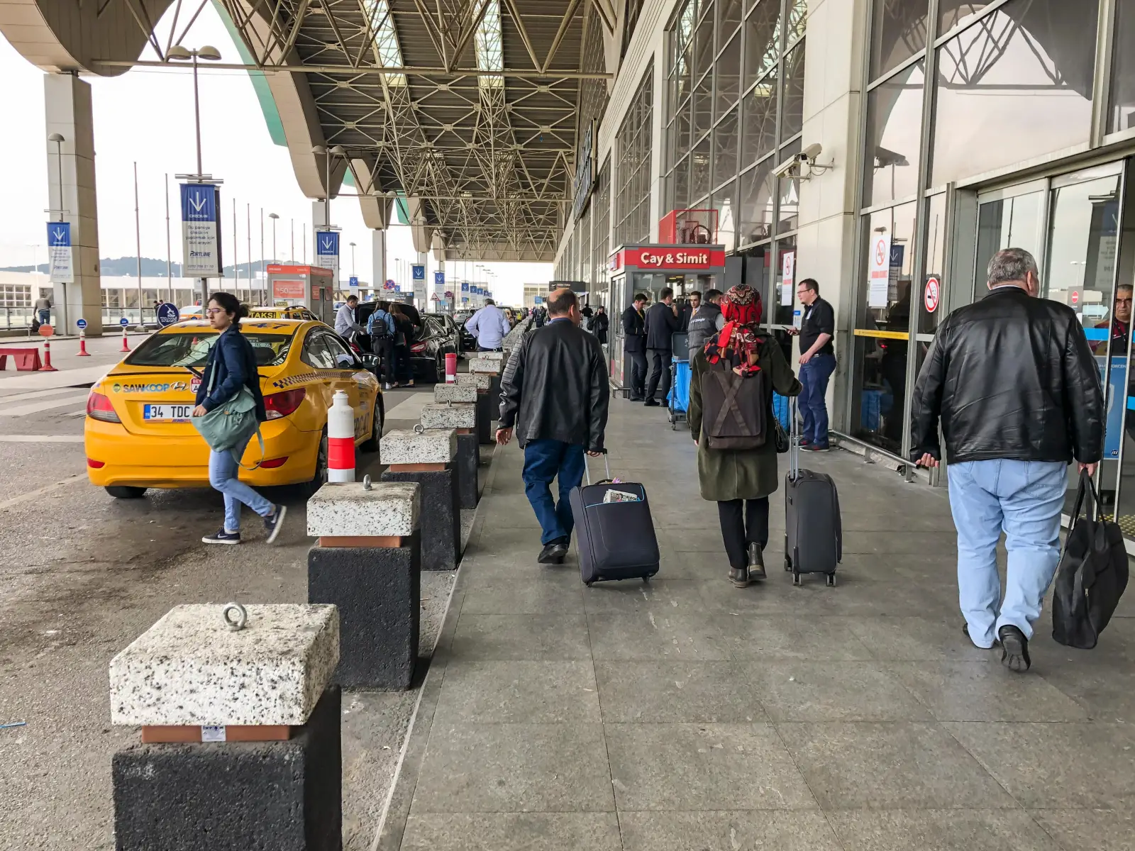 Passengers with luggage walking past taxis at the departures entrance of Sabiha Gokcen Airport in Istanbul