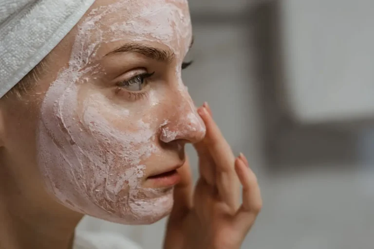 Woman applying pink facial mask with towel wrapped around hair