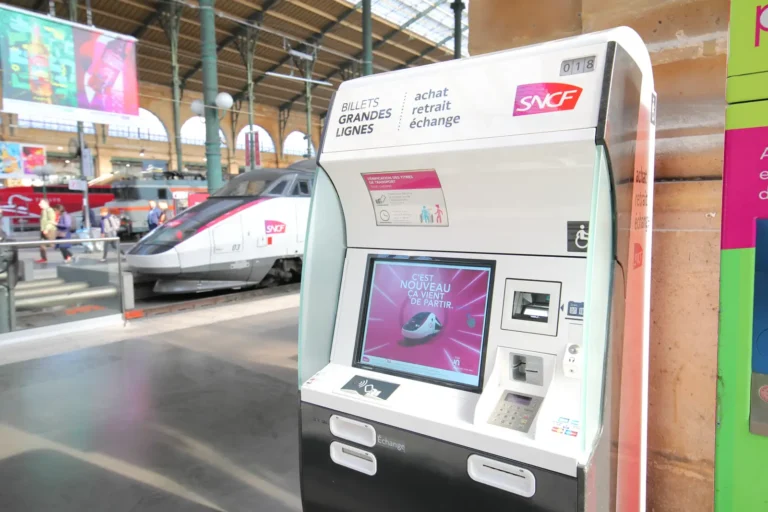 Luxury Travel 28 SNCF ticket machine with a TGV train at a station platform in France.