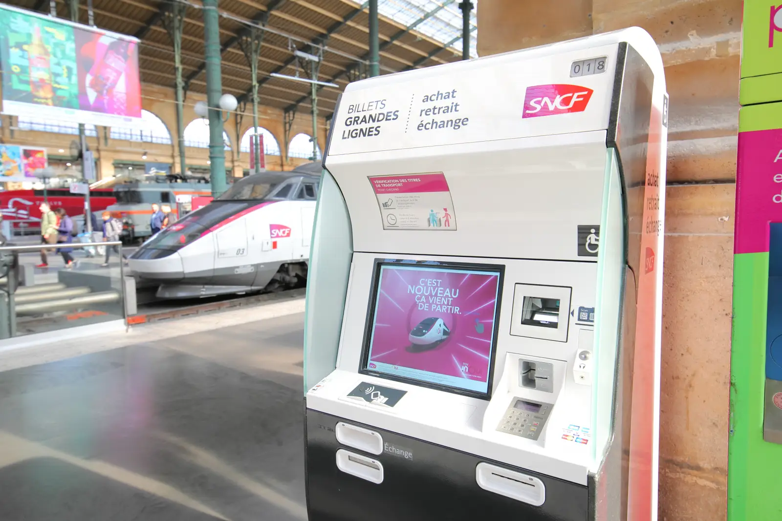 SNCF ticket machine with a TGV train at a station platform in France.