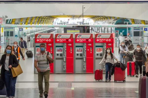 News 46 Travelers wearing face masks walk past Trenitalia ticket machines inside a train station in Italy.