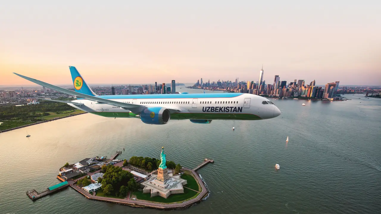 Uzbekistan Airways Boeing 787 Dreamliner flying over the Statue of Liberty with New York City skyline in the background.