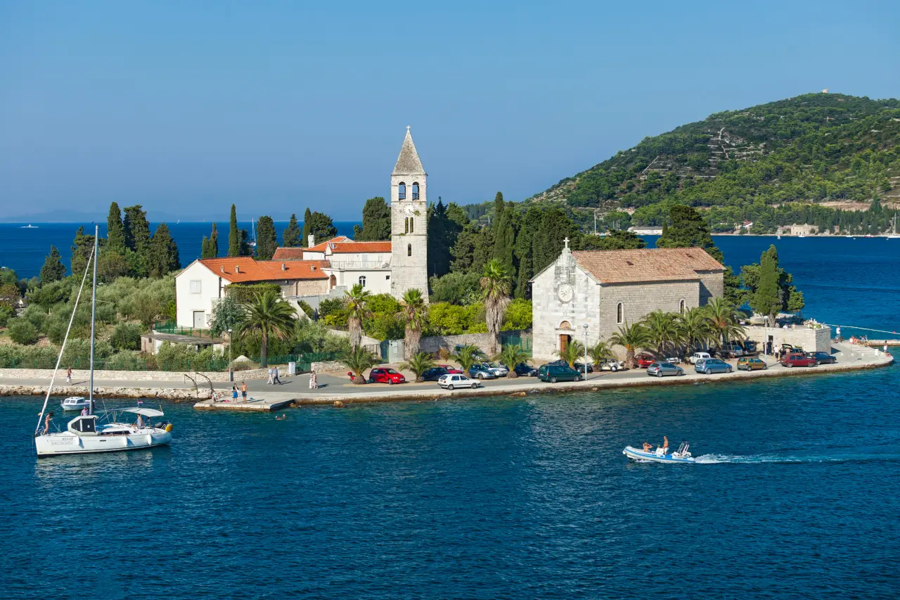 St. Juraj church on Vis Island, Croatia, with stone bell tower, palm trees, and boats in the Adriatic Sea.