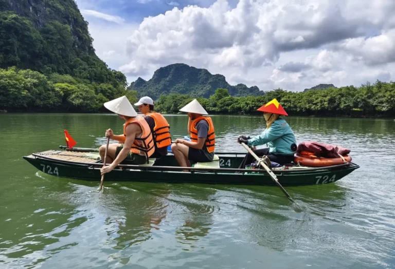 Tourists in life jackets paddling a boat through the calm river at Trang An, Ninh Binh, Vietnam
