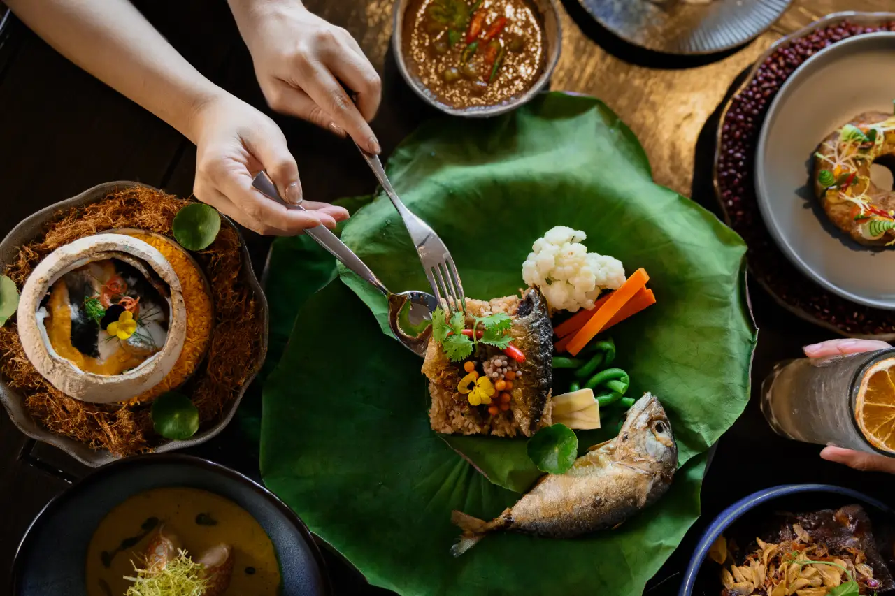 Marriott Unveils Key Trends Redefining Dining Across Asia Pacific 3 Person dining on Asian fusion dishes featuring fish, rice, and vegetables presented on a lotus leaf.