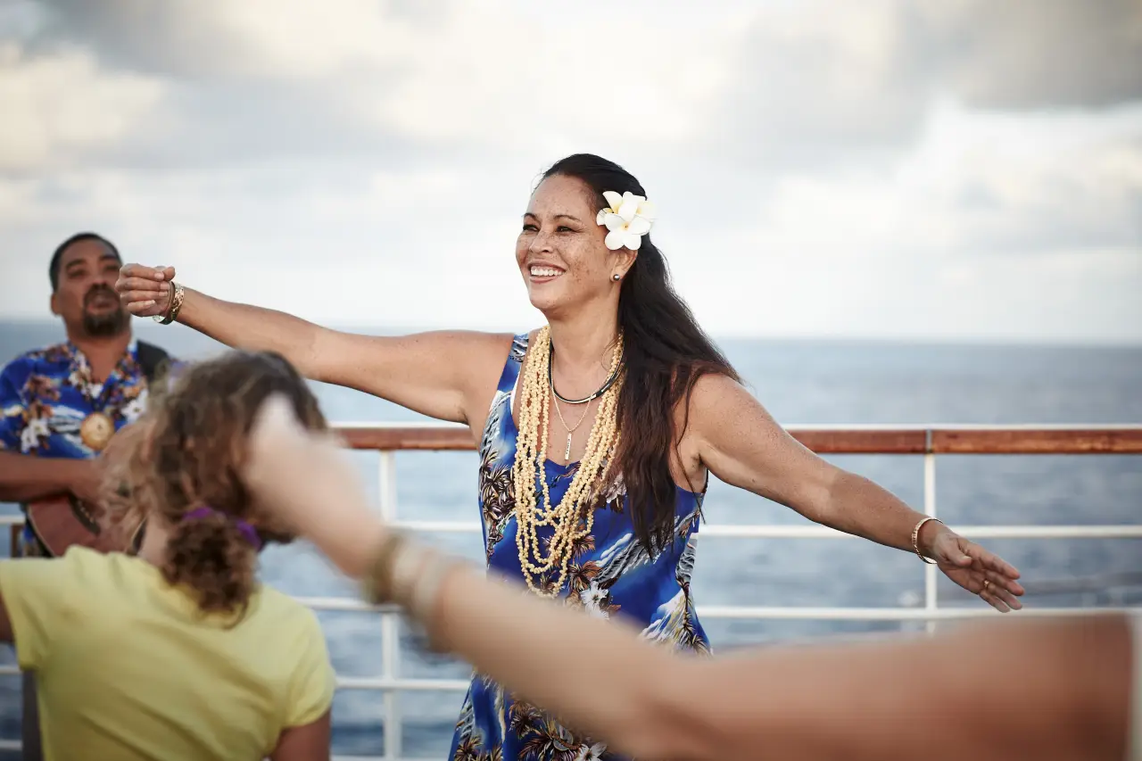 Woman leading a hula dance class on a cruise ship deck with the ocean in the background