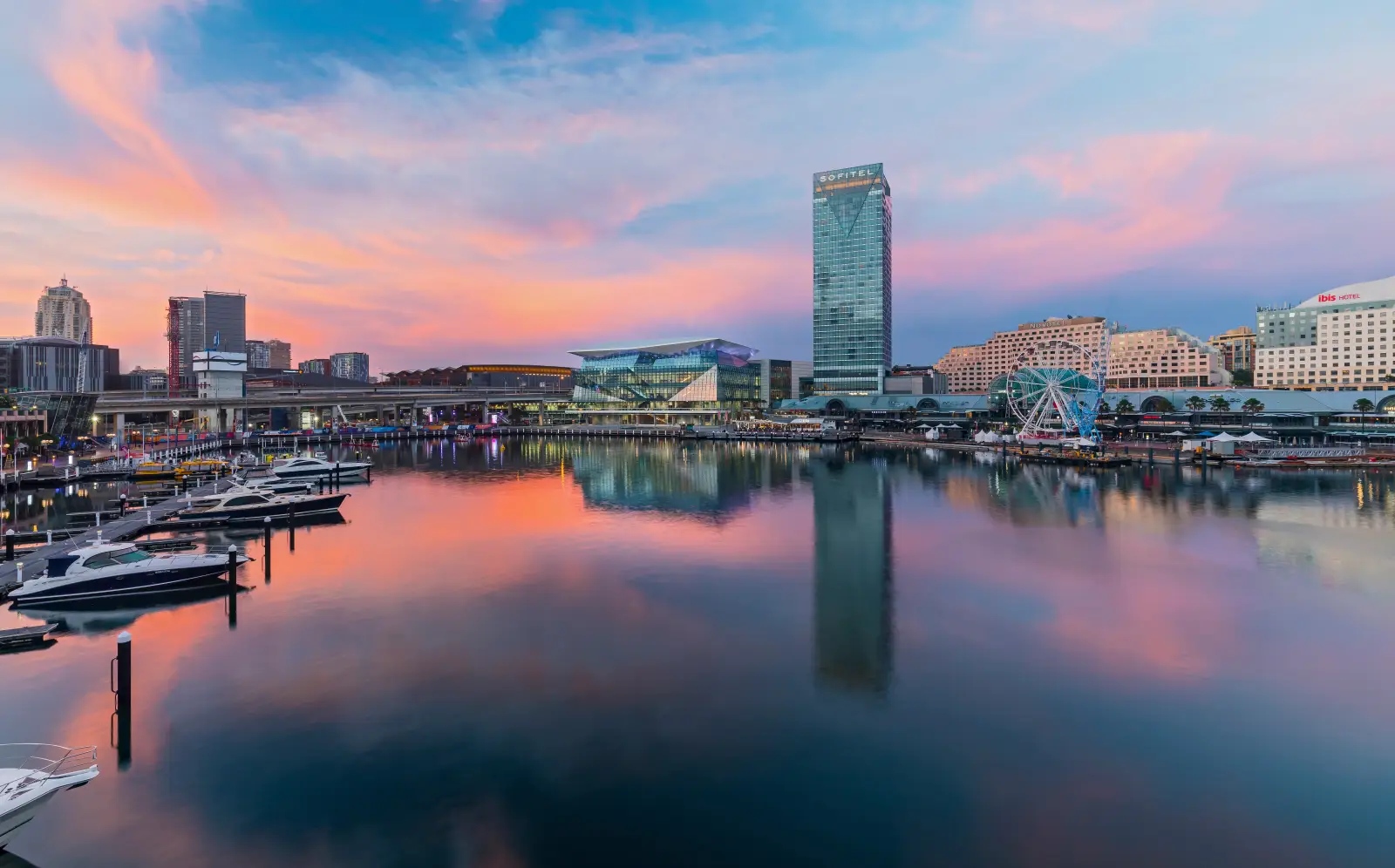 Darling Harbour at sunset featuring ICC Sydney, Sofitel tower, and waterfront yachts.