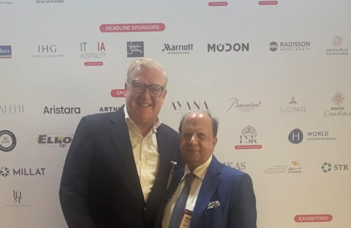 Grand Metropolitan Hotels Expands into UK and India with Signature Hotels Takeover 19 Two business executives posing together at a hospitality industry event in front of sponsor logos.