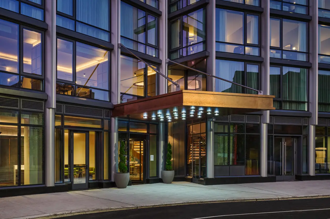 Exterior view of The George at Columbia, Tapestry Collection by Hilton, showing the illuminated entrance and modern glass façade at twilight.
