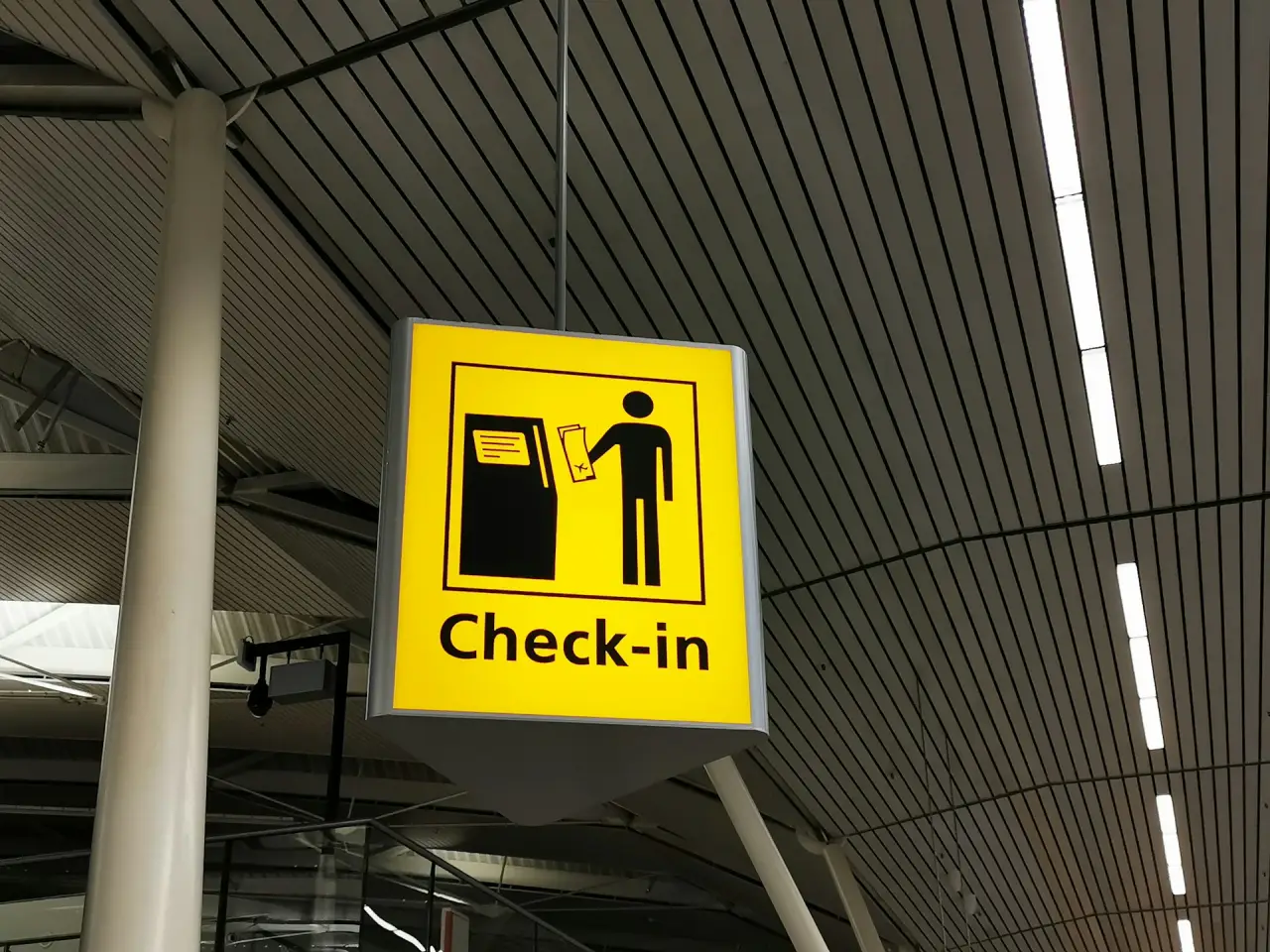 Yellow airport sign showing a person using a kiosk for check-in.