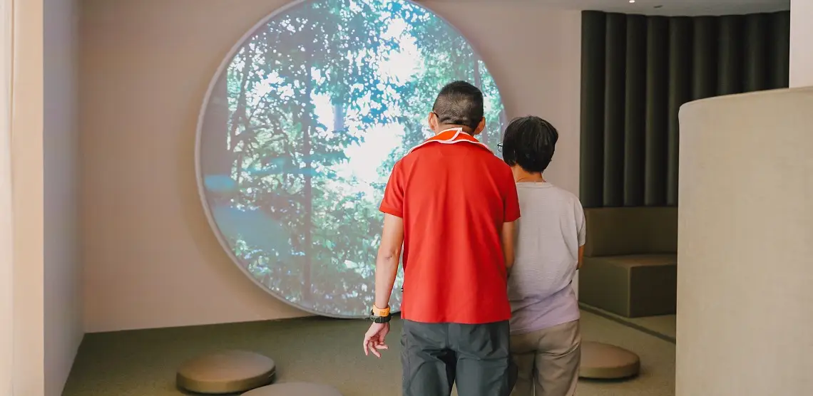 Changi Airport’s Calm Room Welcomes Travellers With Invisible Disabilities 3 Two travellers viewing a forest projection inside Changi Airport’s Calm Room sensory space