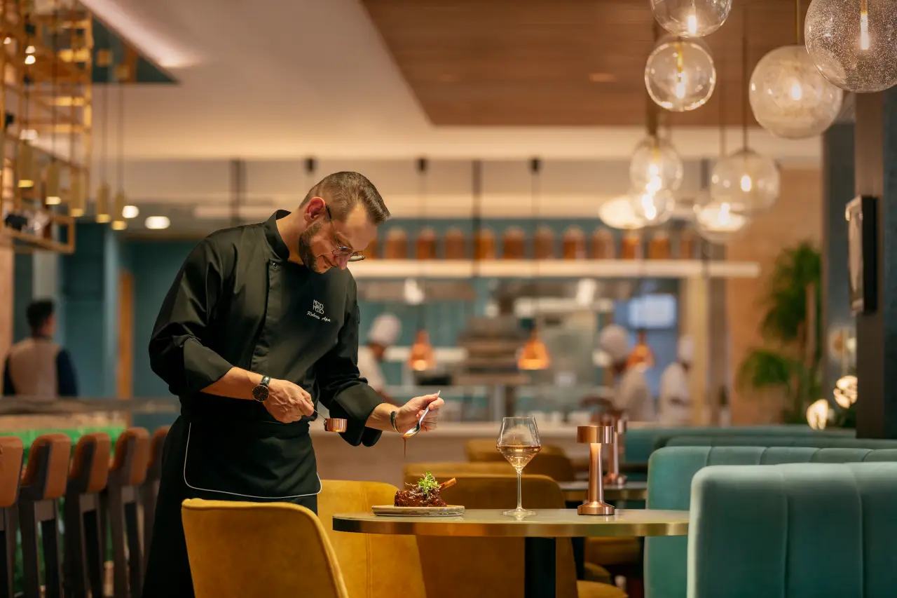 Marriott Unveils Key Trends Redefining Dining Across Asia Pacific 4 Chef plating a dish in a modern restaurant dining room with warm lighting and elegant decor.