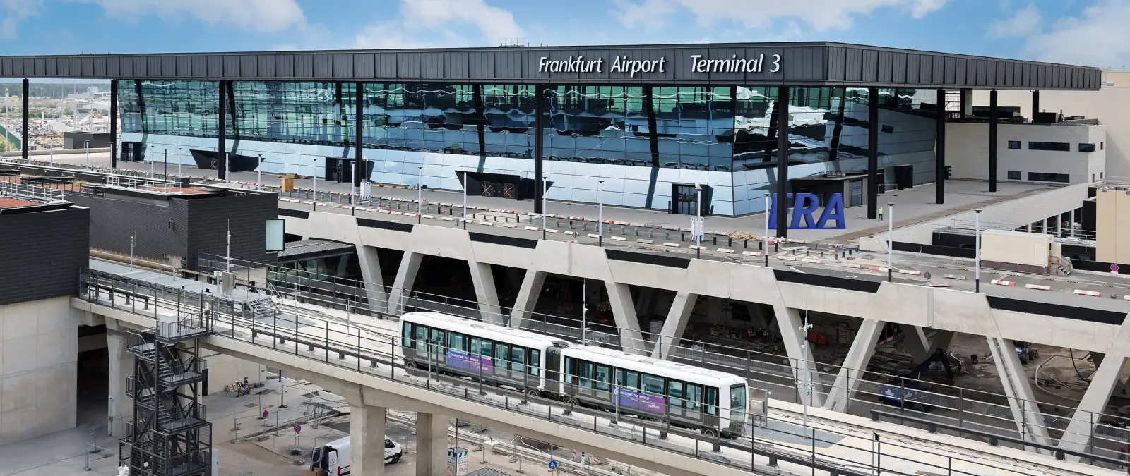 Exterior view of Frankfurt Airport’s new Terminal 3 building with Sky Line train passing in front during final construction phase.