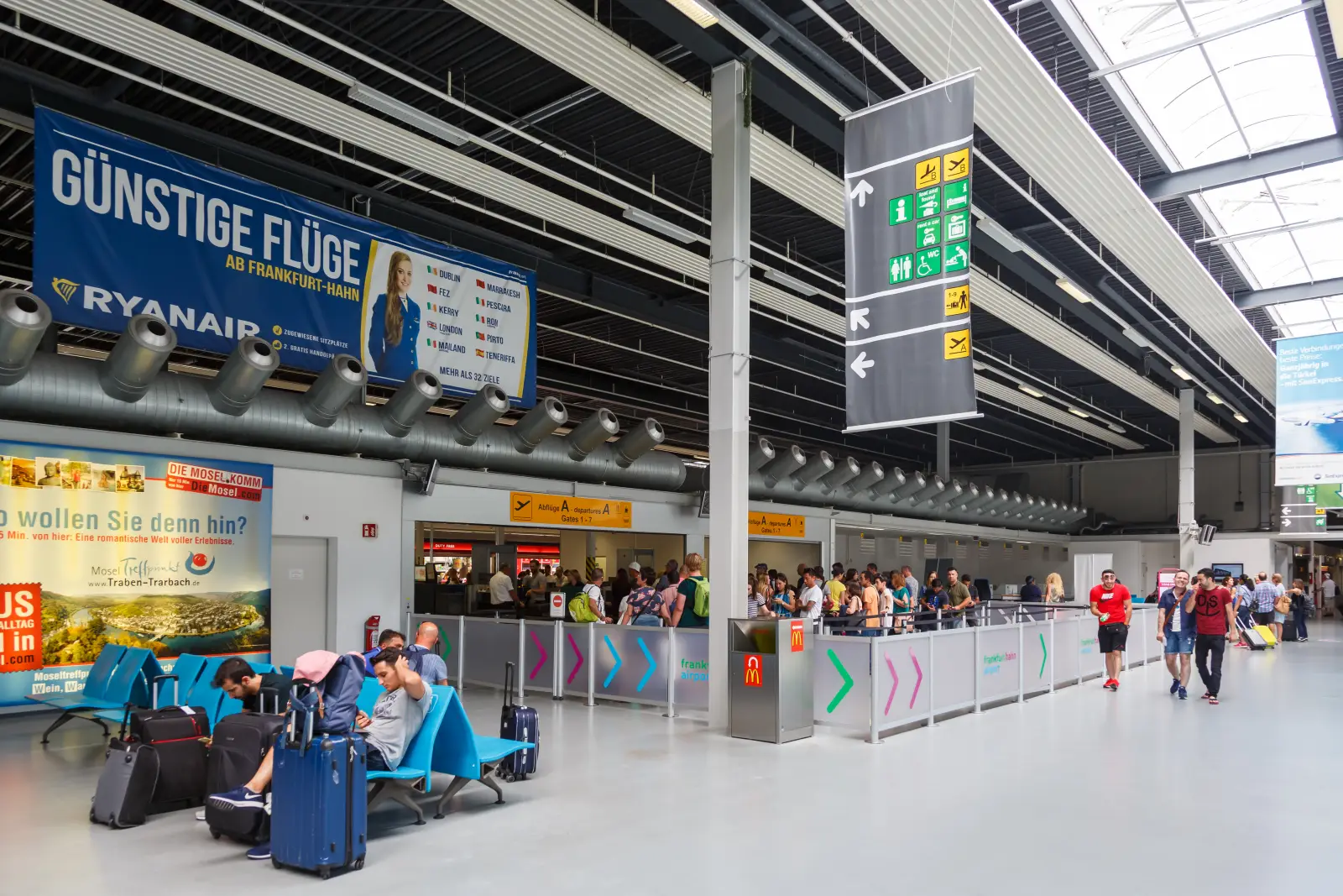 Passengers at Frankfurt-Hahn Airport terminal with Ryanair signage and check-in area in Germany.