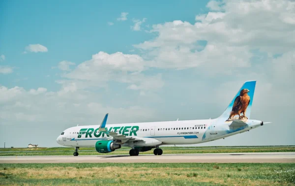 Frontier Airlines aircraft taxiing on a runway under a blue sky, featuring the airline’s signature animal tail design.