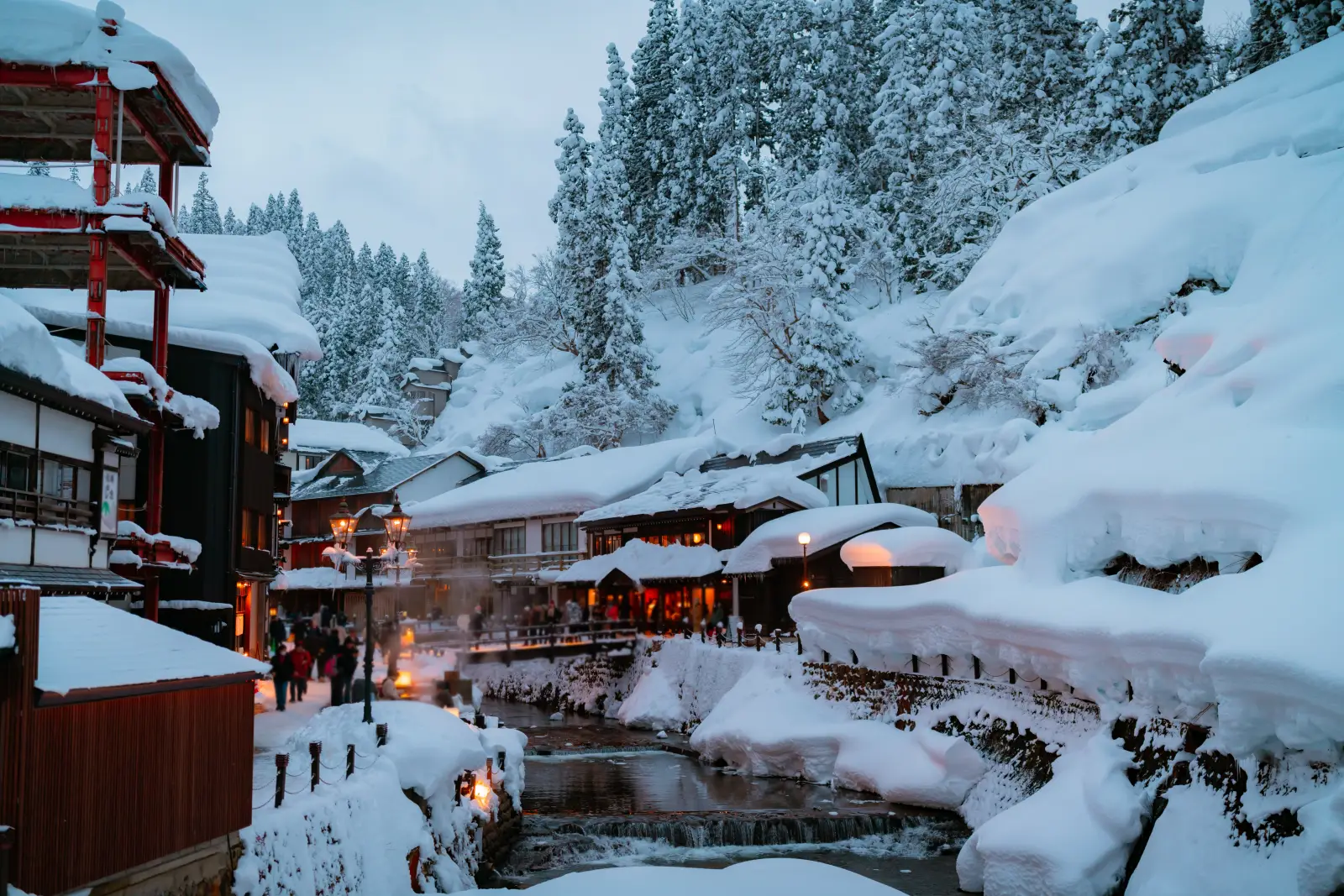 Best Places To Travel In 2026—National Geographic’s Top Picks 4 Snow-covered hot spring village of Ginzan Onsen in Yamagata, Japan, illuminated at dusk with visitors walking along the riverside.