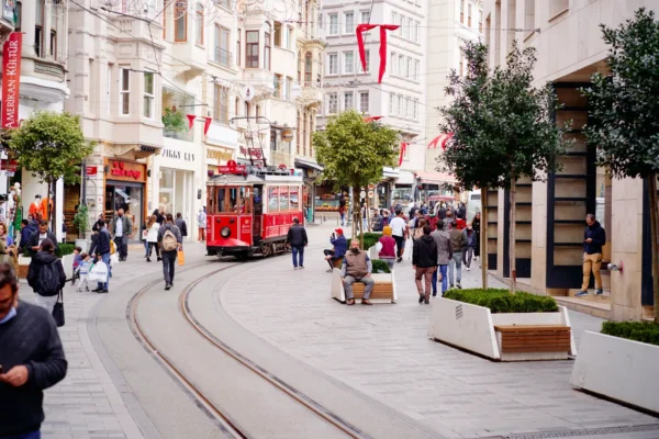 Historic red tram passing through busy Istiklal Street in Istanbul with people walking and shopping.