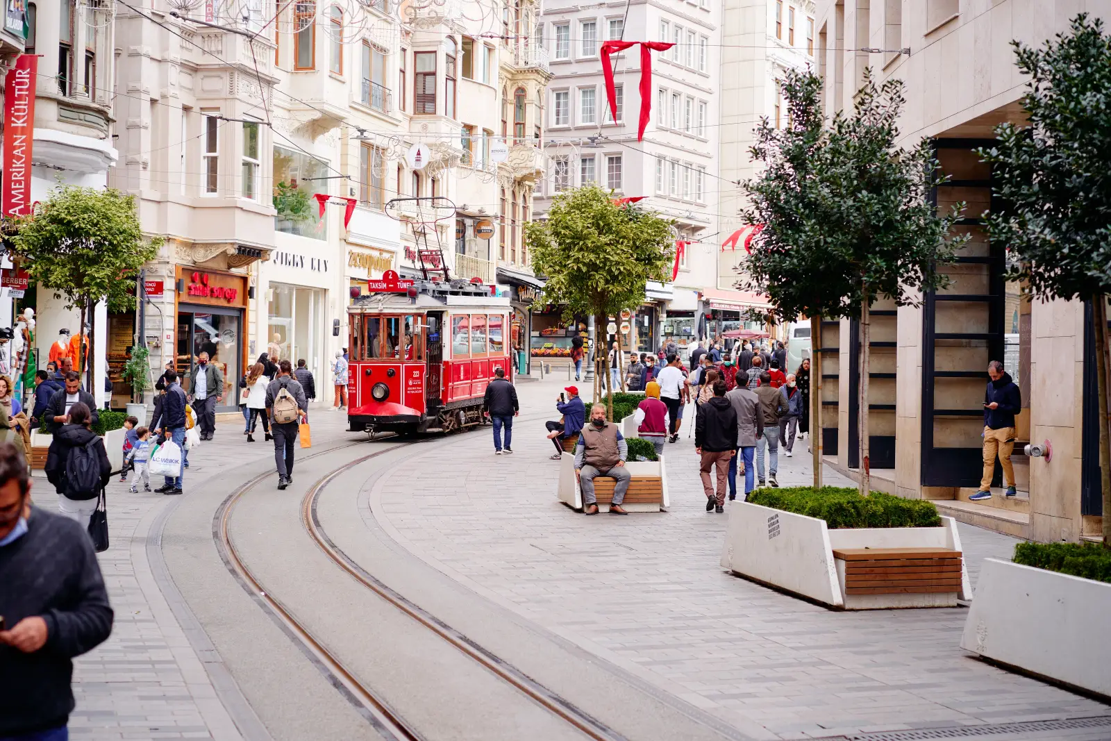 Historic red tram passing through busy Istiklal Street in Istanbul with people walking and shopping.