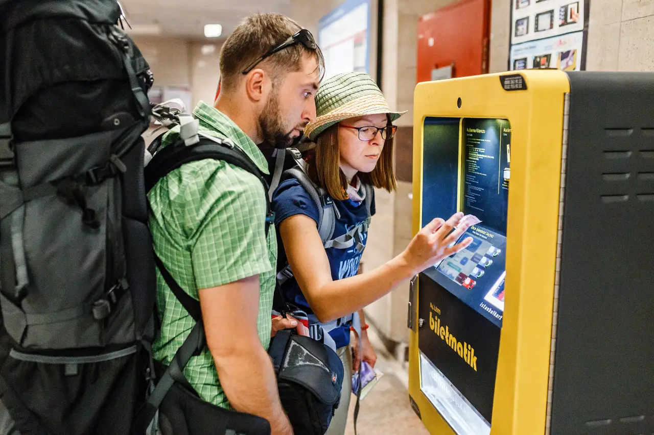 Travelers with large backpacks use a ticket machine at an Istanbul metro station.