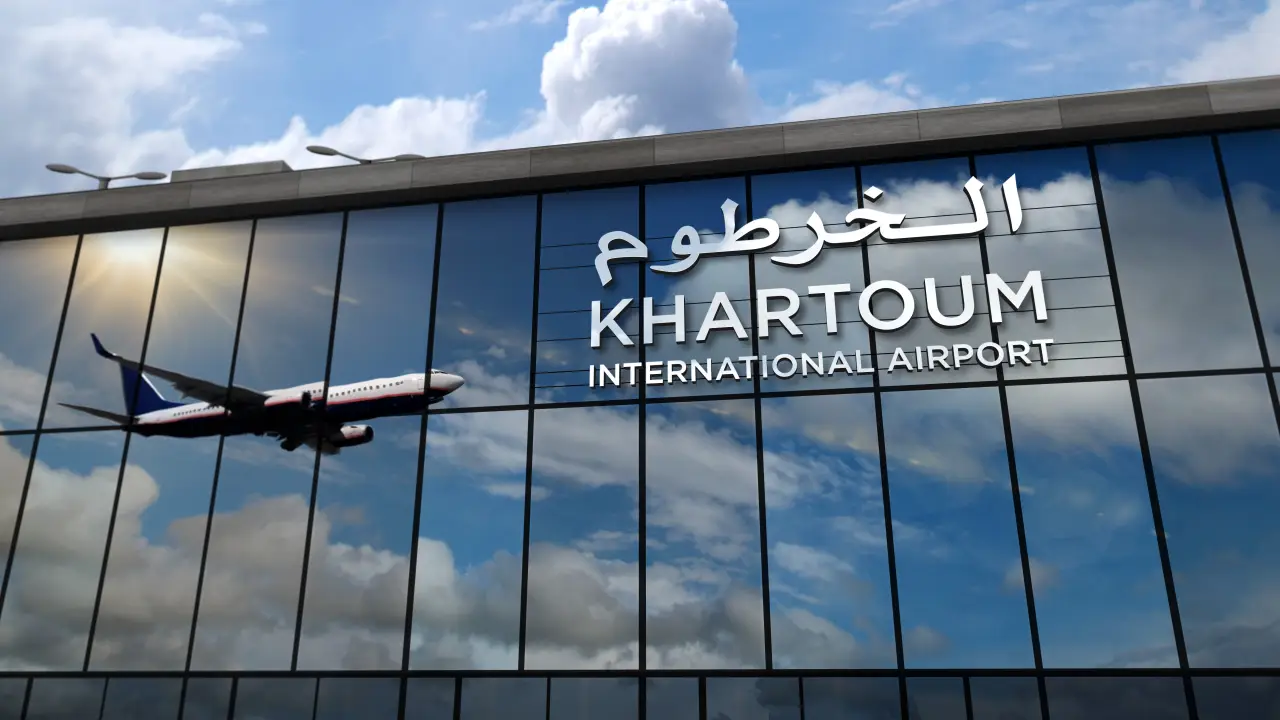 After 921 Days of Silence, Flights Return to Khartoum Airport 33 Airplane reflected on the glass facade of Khartoum International Airport building under a cloudy sky.