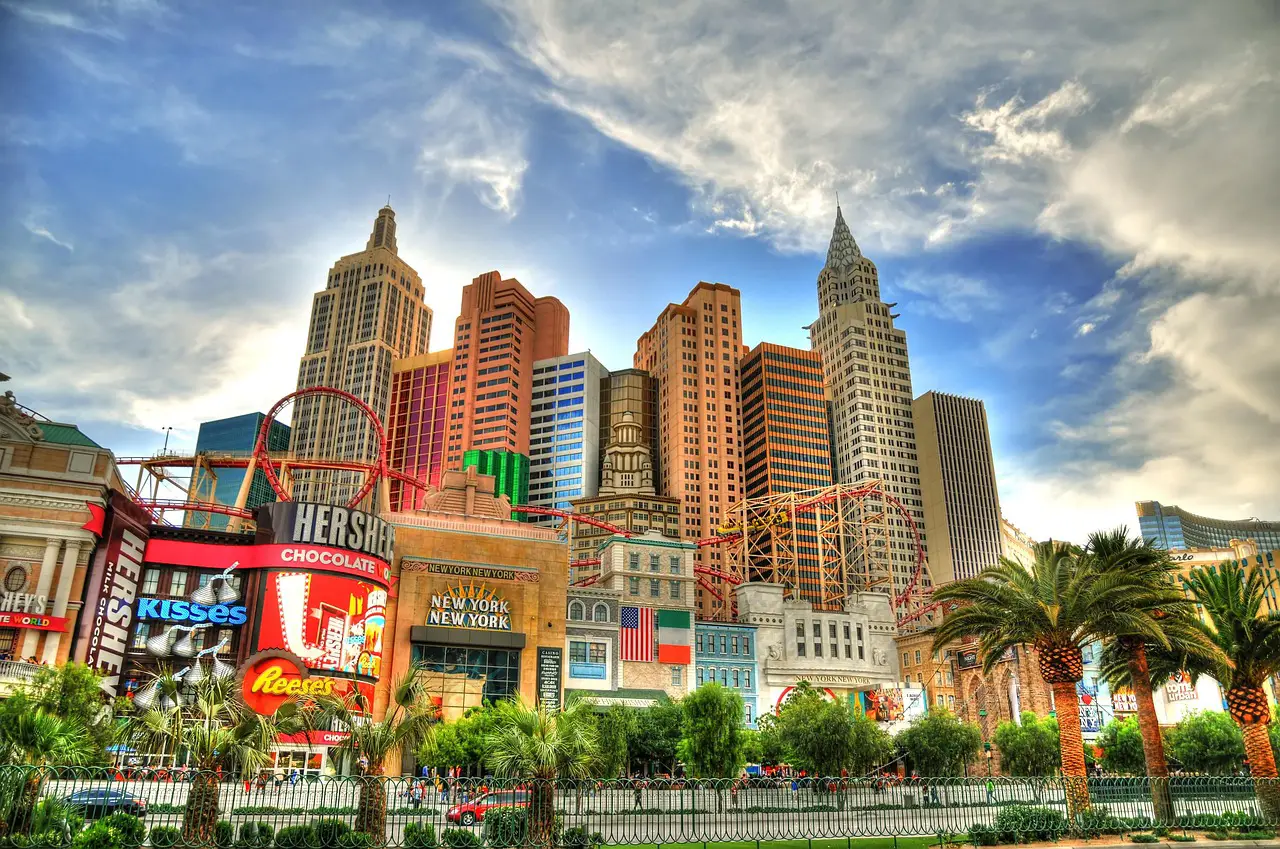 Colorful Las Vegas Strip skyline featuring New York-New York Hotel and Casino with its replica skyscrapers and roller coaster under a bright sky.