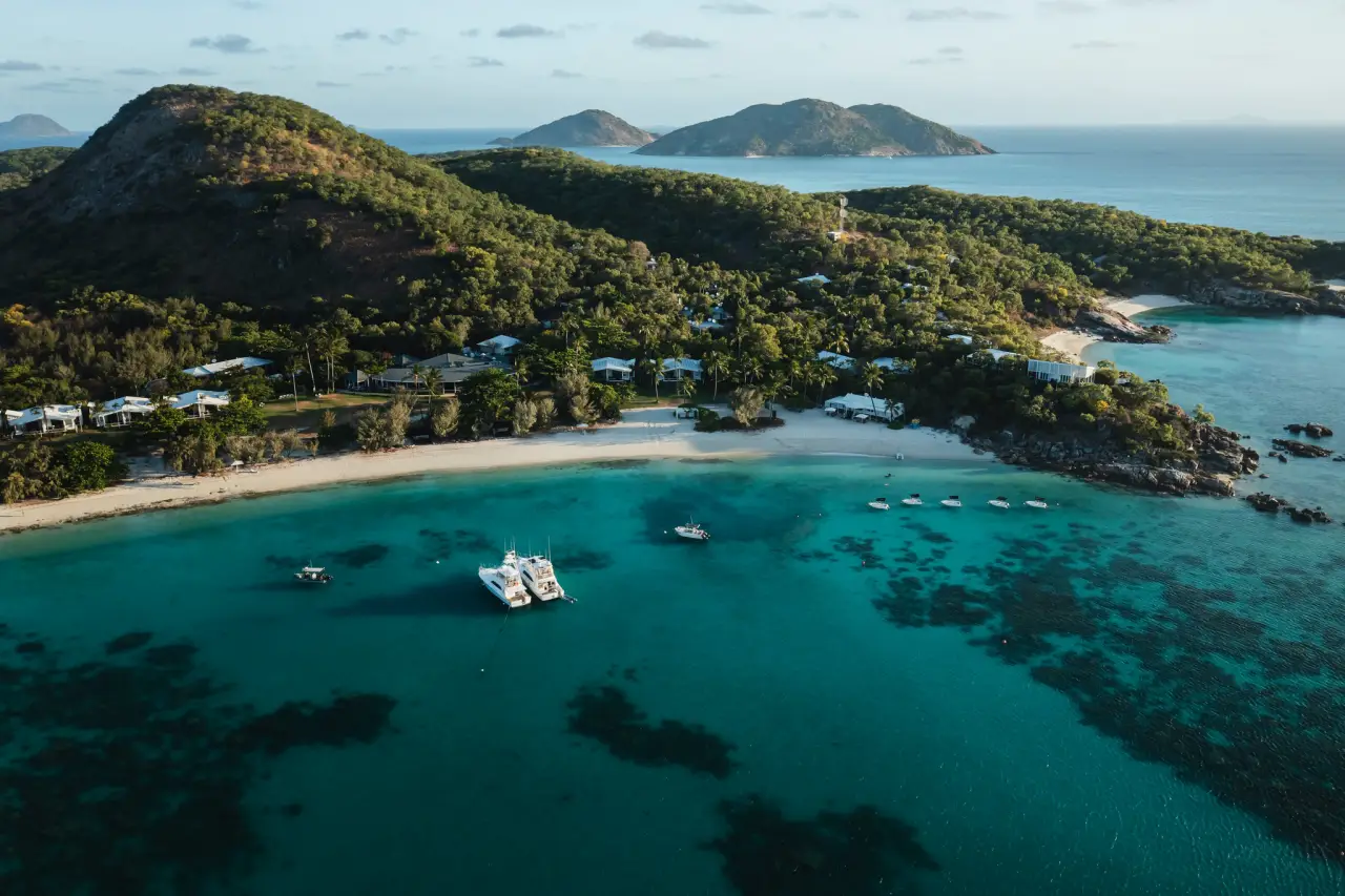 Elderly Cruise Passenger Found Dead After Being Left on Australian Island 12 Aerial view of Lizard Island in Queensland, showing turquoise waters, beaches, and moored boats along the Great Barrier Reef.