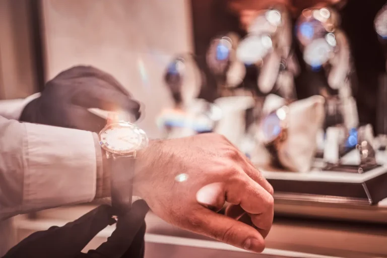 Jewelry store assistant helping a customer try on a luxury wristwatch.