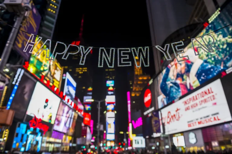 Happy New Year banner hanging above Times Square lights at night in New York City.