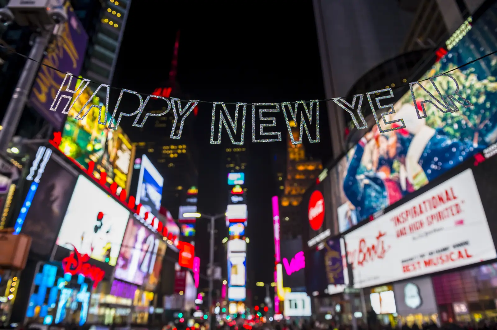 Happy New Year banner hanging above Times Square lights at night in New York City.