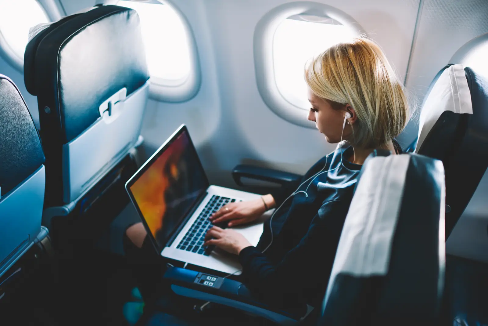 Passenger using a laptop on a reclined airplane seat by the window during a flight.