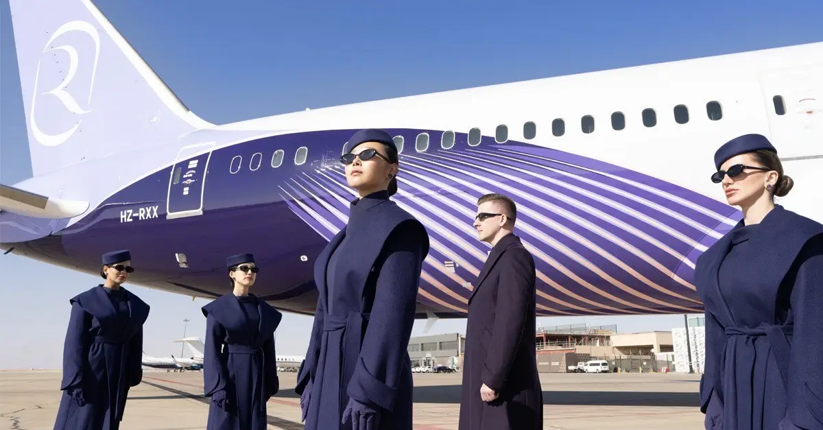 Riyadh Air Announces Inaugural London Flight On October 26 And Sfeer Loyalty Programme 6 Riyadh Air cabin crew in navy uniforms stand beside a Boeing 787 aircraft featuring the airline’s purple livery at an airport.