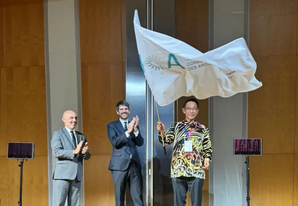 Sarawak to Host ICA Conference 2027 38 Sarawak’s Minister for Tourism, Creative Industry and Performing Arts waves the ICA flag during the official handover ceremony in Barcelona, with two officials applauding beside him.