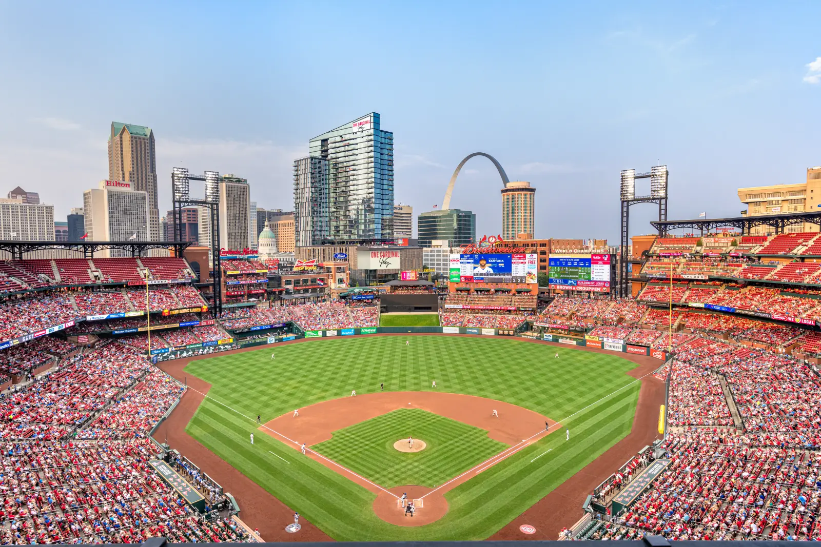 Crowd-filled baseball stadium in St. Louis with city skyline and Gateway Arch in the background.