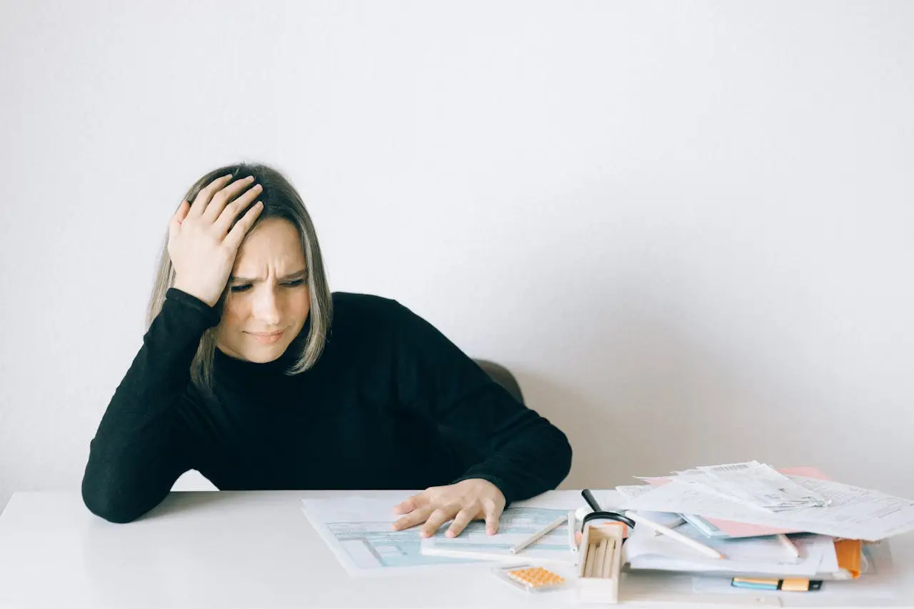 Frustrated woman looking at bills and financial documents at a desk.