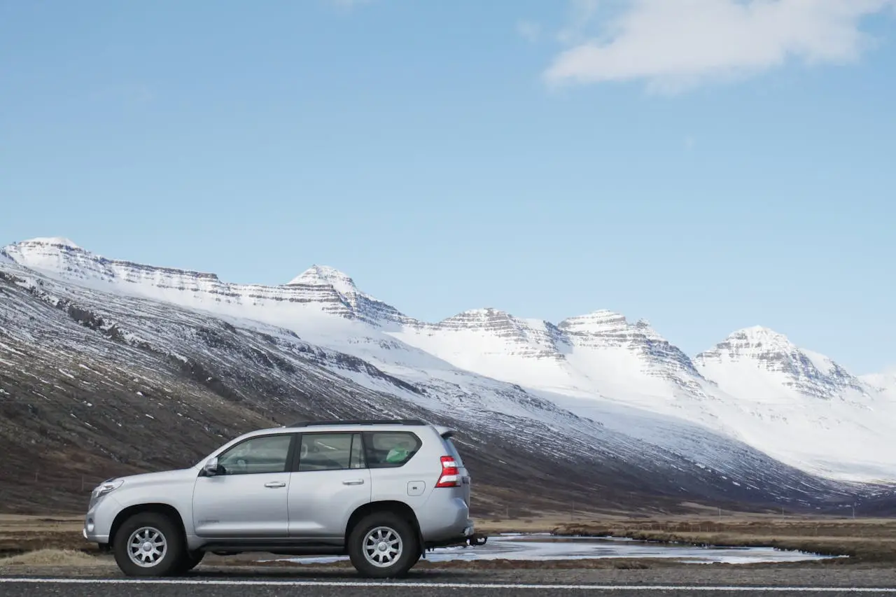 Silver SUV parked on a road with snow-covered mountains in the background under a clear blue sky.
