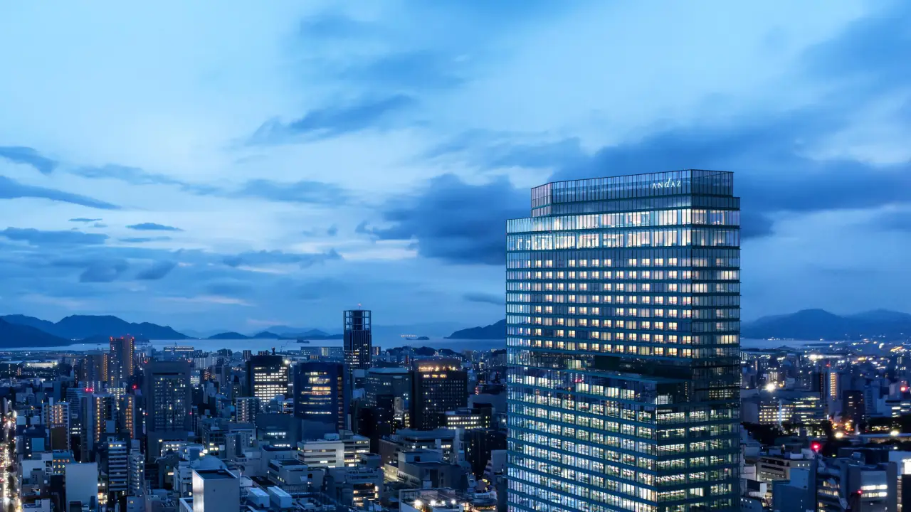 Hyatt To Debut Its First Andaz Hotel In Hong Kong In 2027 As Part Of Expansion Plans In Asia 3 Andaz Hiroshima tower illuminated at dusk overlooking the city skyline and distant sea.