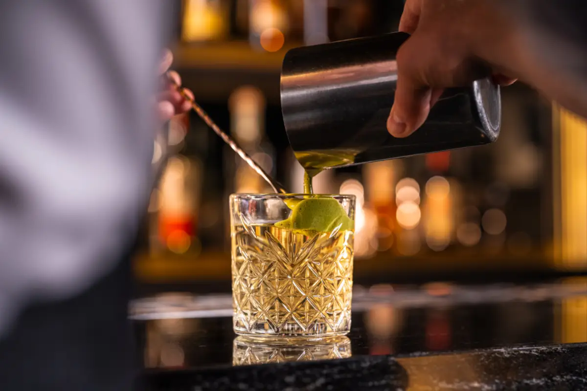 Bartender pouring a matcha-infused Green Tea cocktail into a crystal glass at a bar.