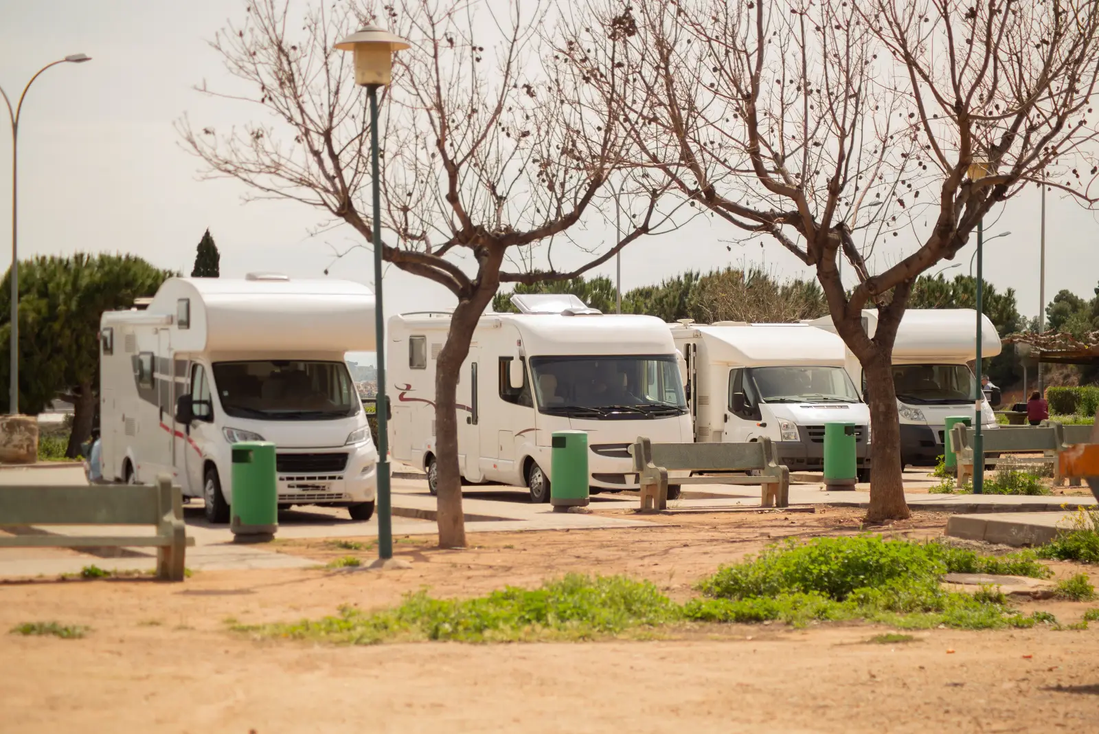 Everything You Need To Know Before Your First Campervan Road Trip 2 Row of campervans parked at a campsite with trees and benches in the foreground.