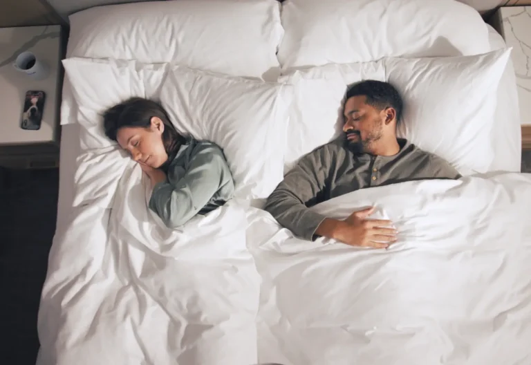 Couple peacefully sleeping in a cozy hotel bed with white linens.