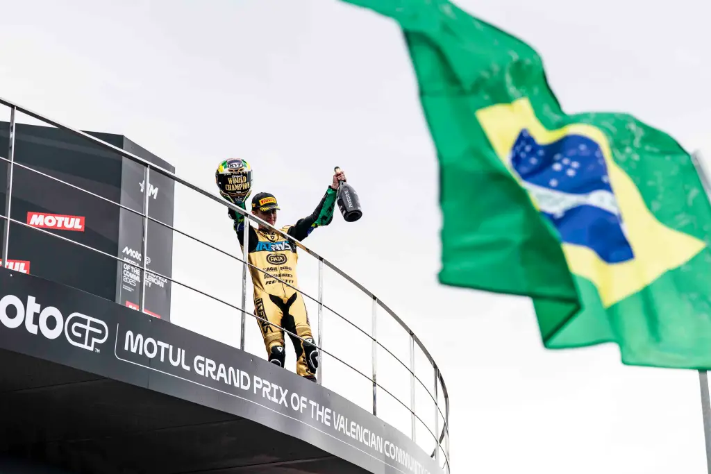 A Dramatic Finale In Valencia Shakes Up The Motogp Season 3 Moto2 champion Diogo Moreira celebrates on the podium at the Valencia Grand Prix with a helmet and champagne as the Brazilian flag waves nearby.