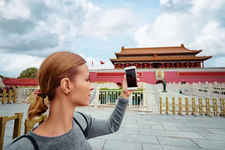 Woman taking a photo with her smartphone in front of the Forbidden City in Beijing, China.