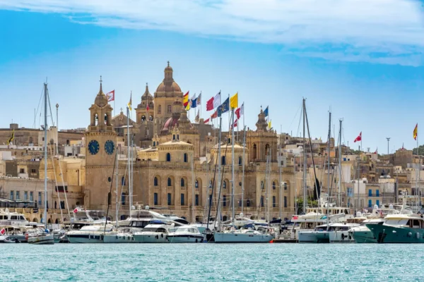 Home 1 Birgu and Vittoriosa skyline in Malta with historic limestone buildings, church domes and a marina of anchored boats.