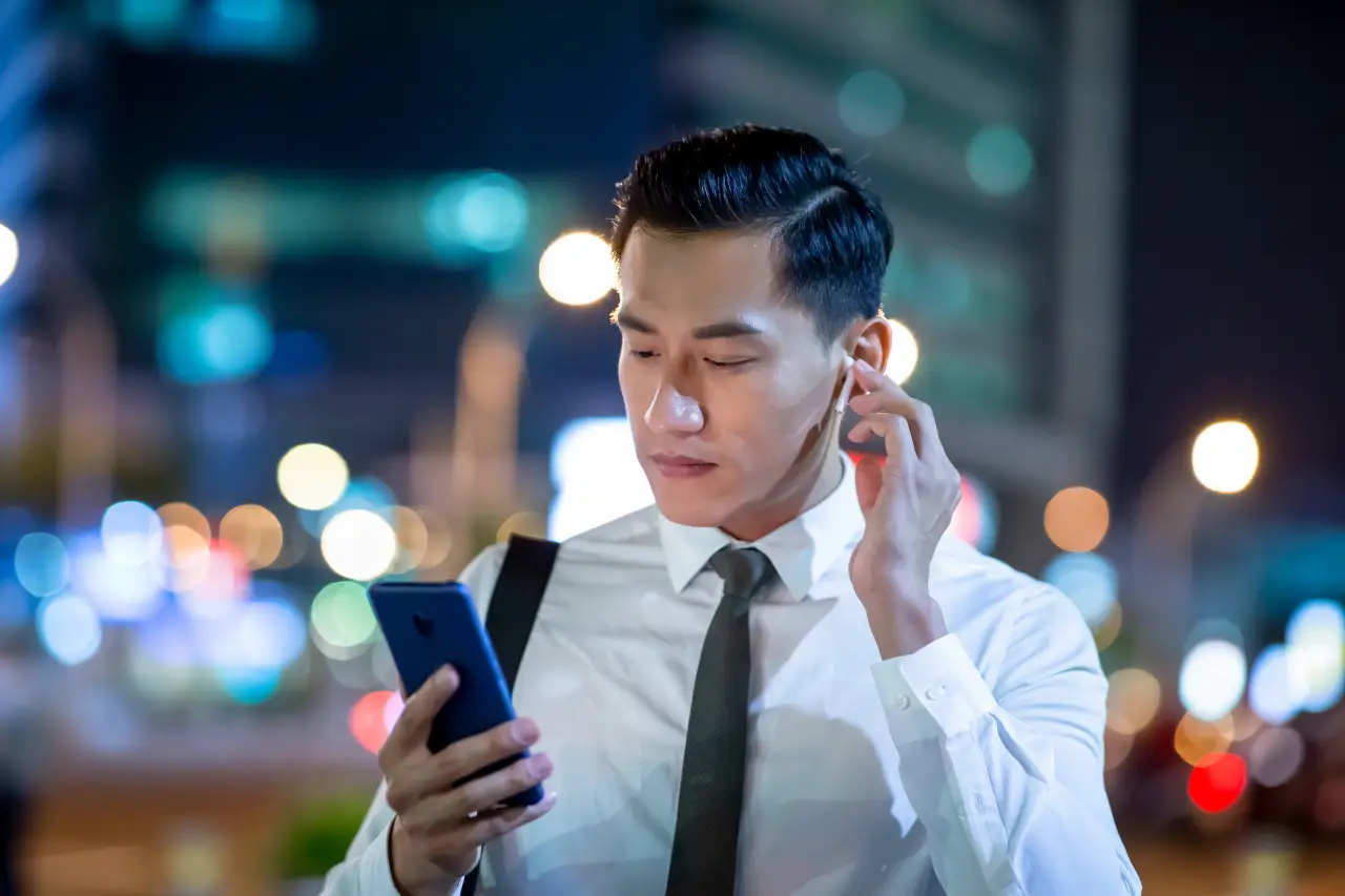 Man using wireless earbuds and smartphone on a city street at night.