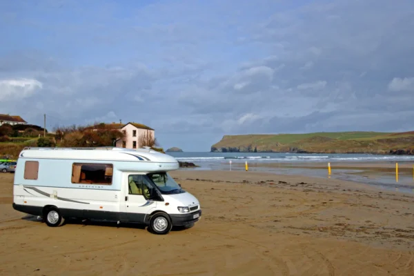 Motorhome parked on Polzeath Beach with waves and coastal cliffs in Cornwall.