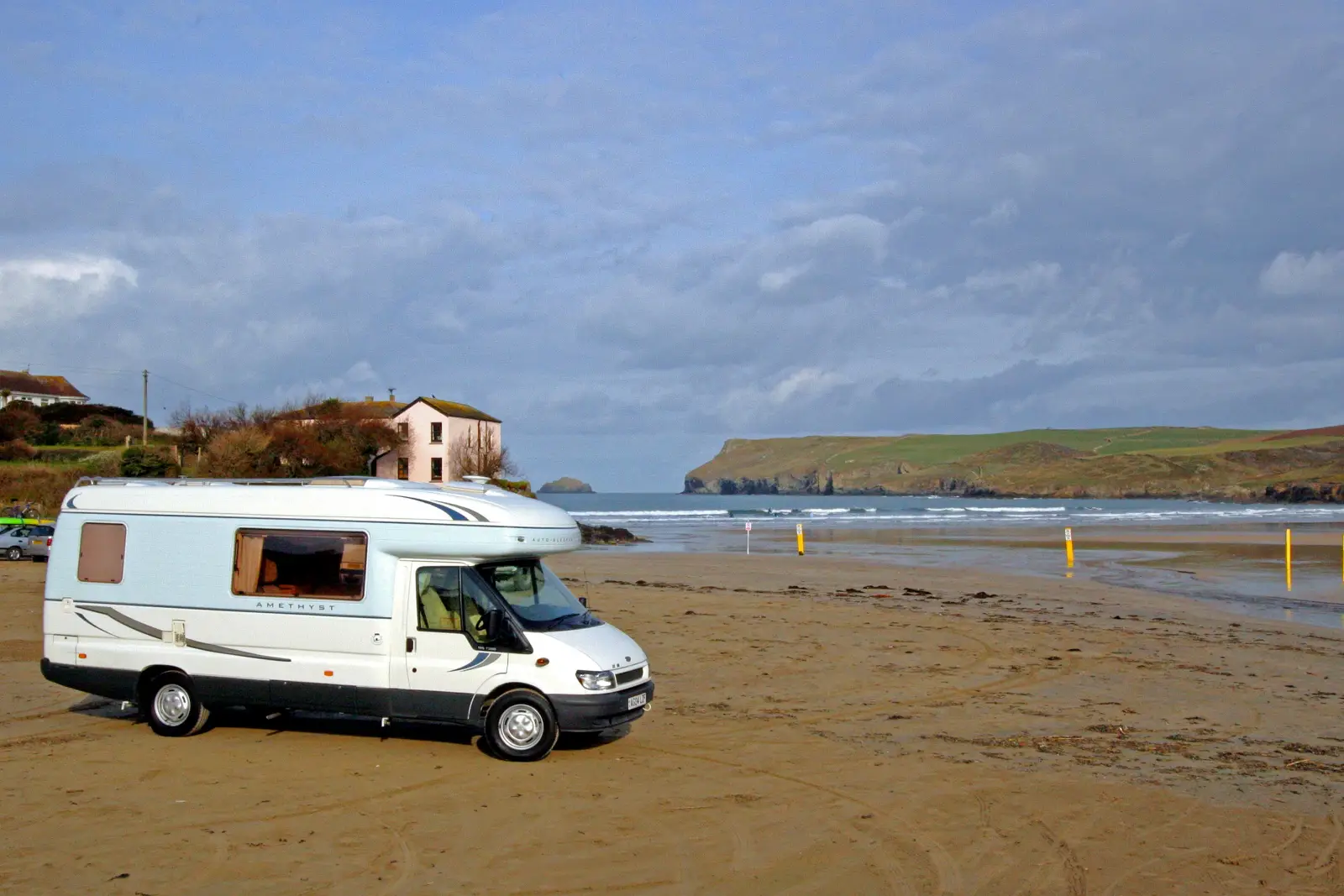 Motorhome parked on Polzeath Beach with waves and coastal cliffs in Cornwall.