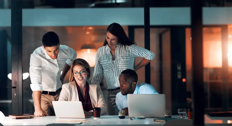 Technology 11 Team of professionals collaborating around a laptop in a modern office at night.