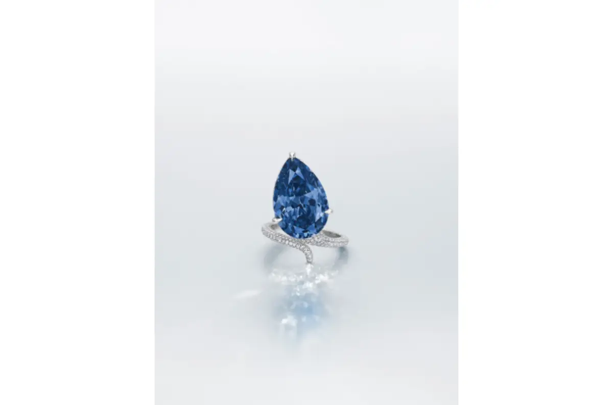 Vivid blue pear-shaped diamond ring displayed on a reflective surface