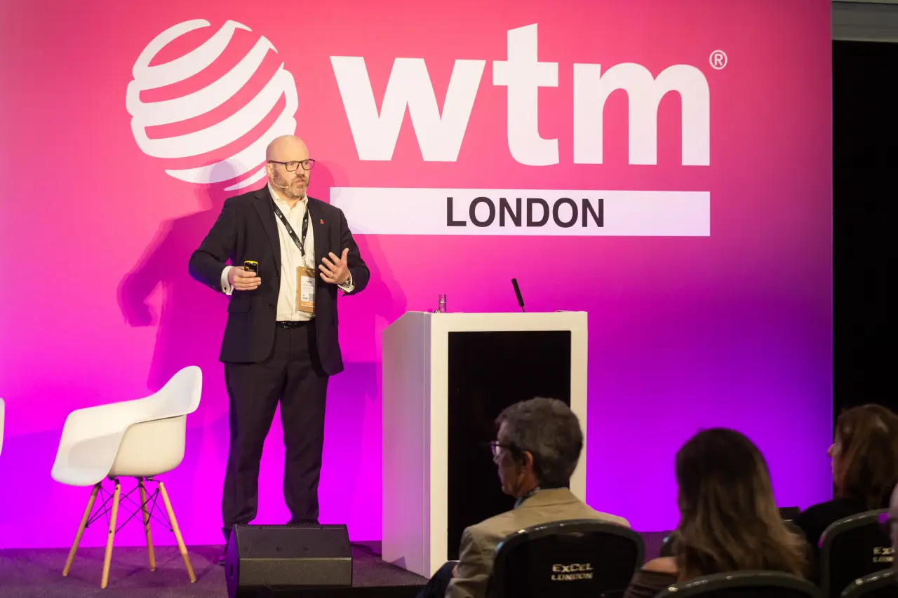 Speaker presenting during a session at World Travel Market London with WTM logo in the background.